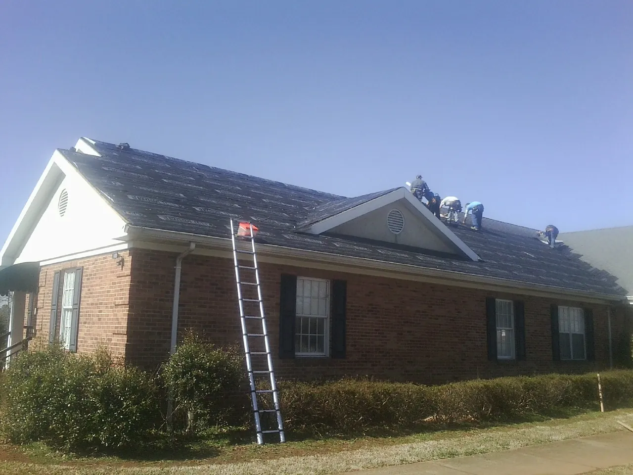 Crew tearing shingles off a brick ranch roof with a ladder set — Emergency Roof Repair work by our crew in Nicholls