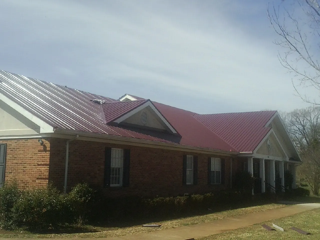 Red metal roof with gabled entries on a long brick building, from a Hail Damage Roof Repair job in Nicholls