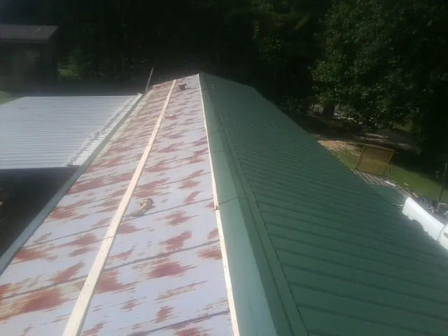 Old rusted panels beside newly installed green metal roofing — Wind Damage Roof Repair by Roofing Brothers in Nicholls