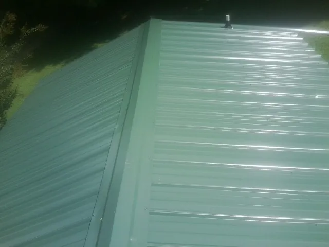 New green metal panels meeting at the ridge of a roof — Flat Roof Repair work by our crew in Nicholls