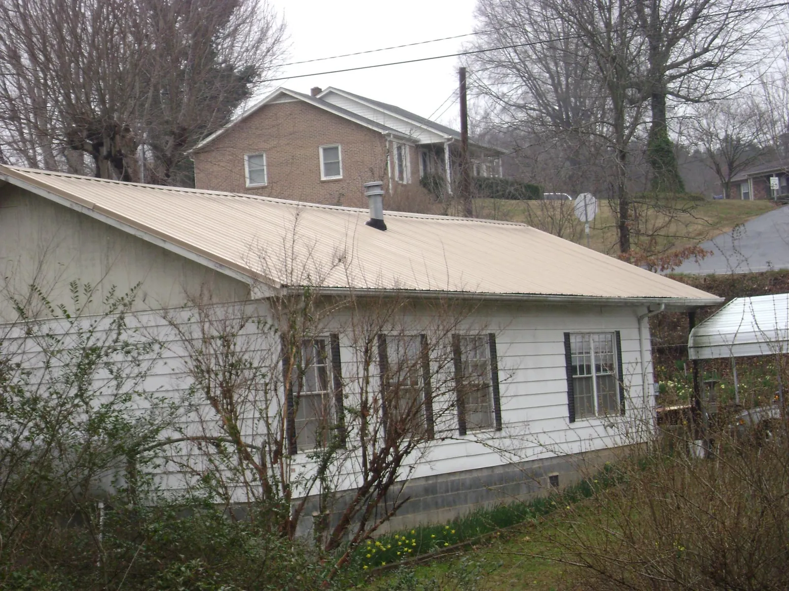 Tan metal roof on a white sided house set into a hillside — Commercial Roofing by Roofing Brothers in Nicholls